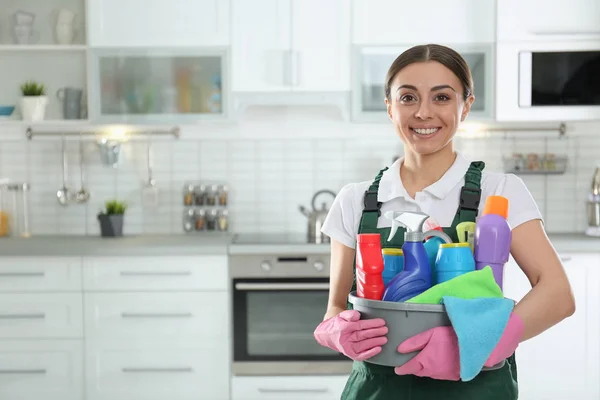 Portret van jonge vrouw met bekken van detergenten in keuken. Schoonmaakservice — Stockfoto