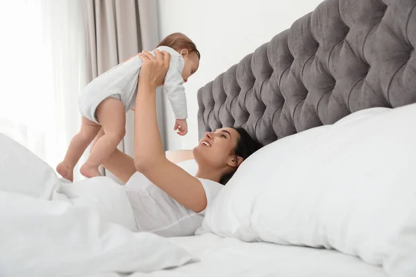Joven madre jugando con su lindo bebé en la cama en el interior —  Fotos de Stock