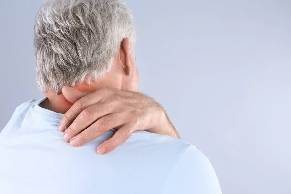 Senior man scratching neck on grey background, space for text. Allergy symptom