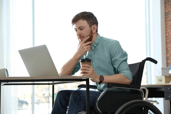 Junger Mann im Rollstuhl benutzt Laptop am Arbeitsplatz — Stockfoto
