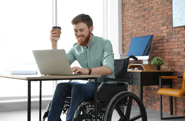 Junger Mann im Rollstuhl benutzt Laptop am Arbeitsplatz — Stockfoto