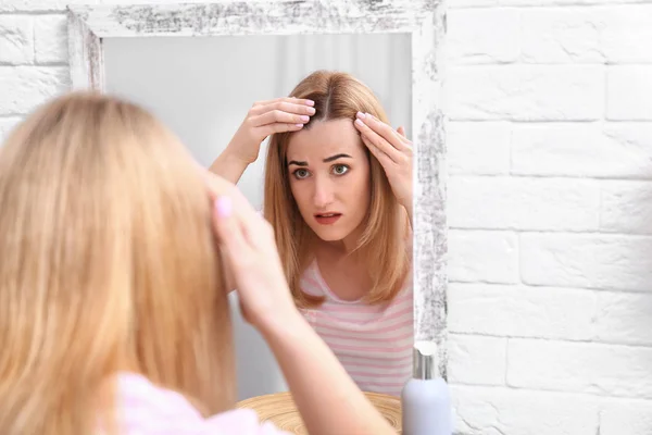 Jonge vrouw met haaruitval probleem in de buurt spiegel binnen — Stockfoto