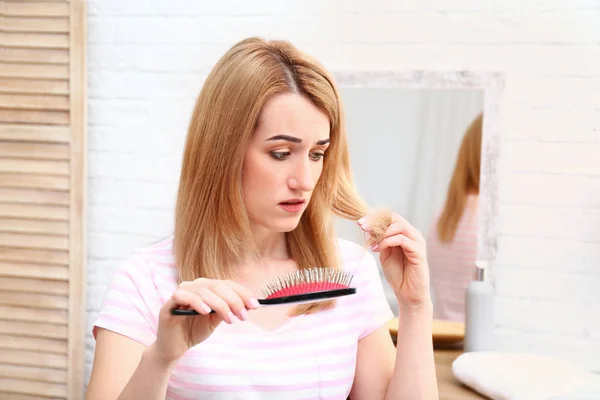 Emotional young woman brushing hair in bathroom — Stock Photo, Image