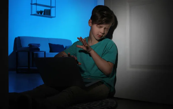 Испуганный маленький ребенок с ноутбуком на полу в темной комнате. Опасность интернета — стоковое фото