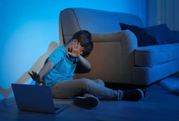 Frightened little child with laptop on floor in dark room. Danger of internet