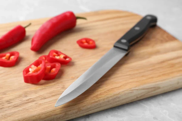 Wooden board with sharp knife and cut chili peppers on table, closeup