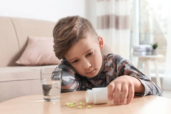 Маленький ребенок с таблетками и водой за столом в помещении. Опасность интоксикации лекарствами — стоковое фото