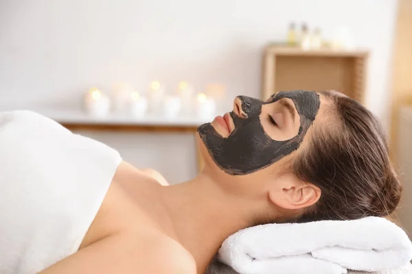 Mulher bonita com máscara preta no rosto relaxante no salão de spa — Fotografia de Stock