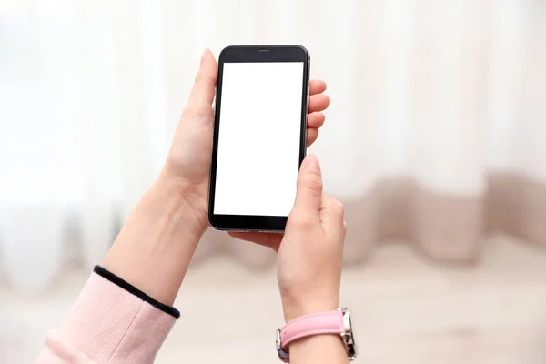 Kobieta trzyma smartfon z pustym ekranem w pomieszczeniu, zbliżenie rąk. Miejsce na tekst — Zdjęcie stockowe