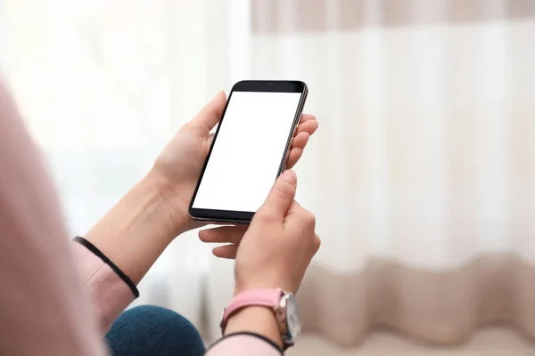 Mulher segurando smartphone com tela em branco dentro de casa, close-up de mãos. Espaço para texto — Fotografia de Stock