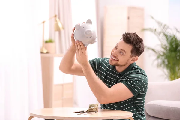 Man with piggy bank and money at home — Stock Photo, Image