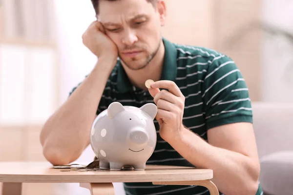 Smutny człowiek z Piggy Bank i pieniądze w domu — Zdjęcie stockowe