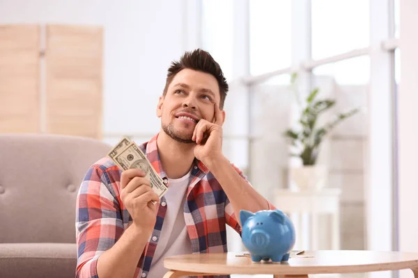 Man with piggy bank and money at home — Stock Photo, Image