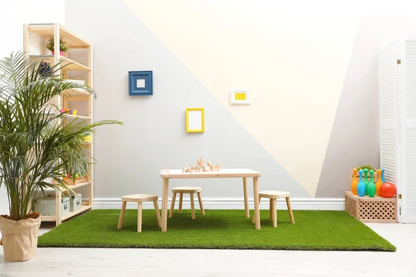 Κομψό εσωτερικό σε αίθουσα παιχνιδιών με τραπέζι, σκαμπό και πράσινο χαλί — Φωτογραφία Αρχείου