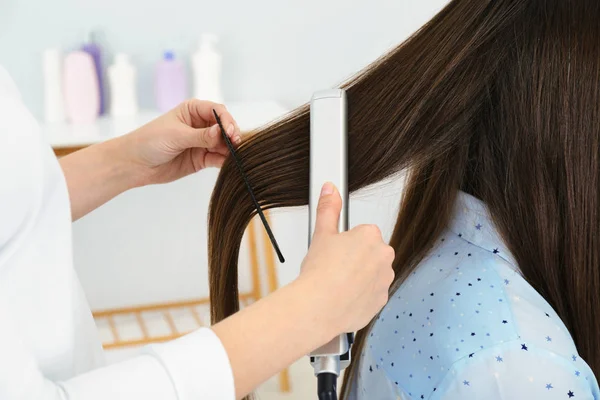 Kadeřník, který používá moderní ploché železo ke stylování vlasů v kadeřnictví, v šatně — Stock fotografie
