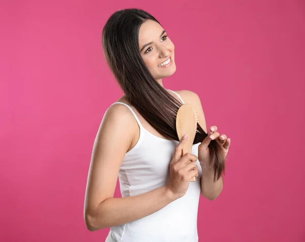 Hermosa joven sonriente con cepillo de pelo sobre fondo de color — Foto de Stock