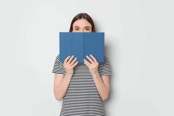 Mujer joven escondida detrás de un libro sobre fondo blanco. Actividad de lectura — Foto de Stock