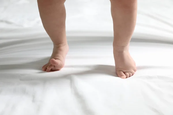 Mignon petit bébé debout sur drap de lit blanc, gros plan — Photo