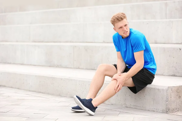 Homem de sportswear sofrendo de dor no joelho nas escadas — Fotografia de Stock