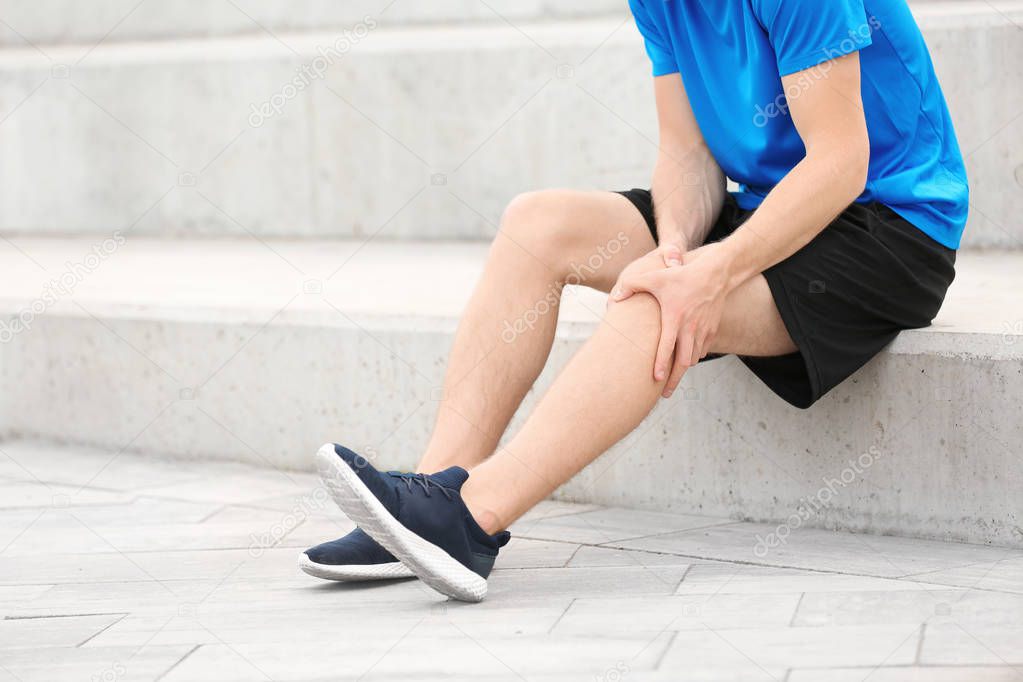 Man in sportswear suffering from knee pain on stairs, closeup
