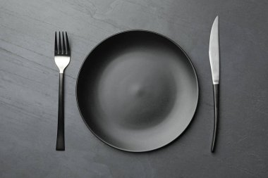 Koyu arka planda şık seramik plaka ve çatal bıçak takımı, düz yatıyordu