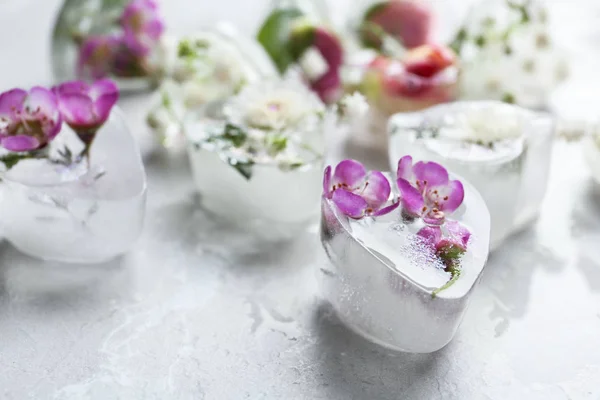 Cubos de hielo en forma de corazón con flores sobre fondo gris, primer plano. Espacio para texto — Foto de Stock