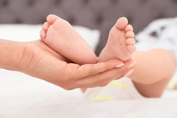 Mamma håller barnets fötter på sängen, närbild — Stockfoto