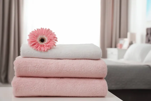 Stack of clean towels with flower on table in bedroom — Stock Photo, Image