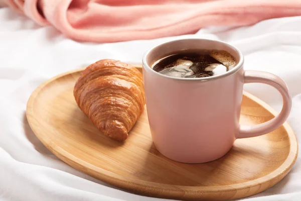 Bandeja de madera con taza de café aromático y croissant sobre tela blanca. Desayuno en la cama —  Fotos de Stock