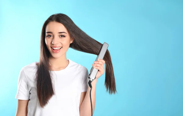 Mulher feliz usando ferro de cabelo no fundo de cor. Espaço para texto — Fotografia de Stock