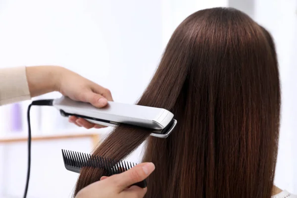 Peluquería usando plancha plana moderna para peinar el cabello del cliente en el salón — Foto de Stock