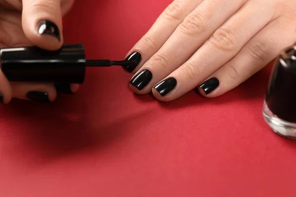 Woman applying black nail polish on color background, closeup