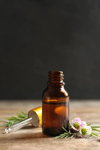 Fles natuurlijke Tea tree olie en plant op tafel tegen donkere achtergrond — Stockfoto