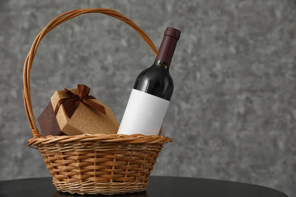 Плетеная корзина с бутылкой вина и подарочной коробкой на столе. Пространство для дизайна — стоковое фото