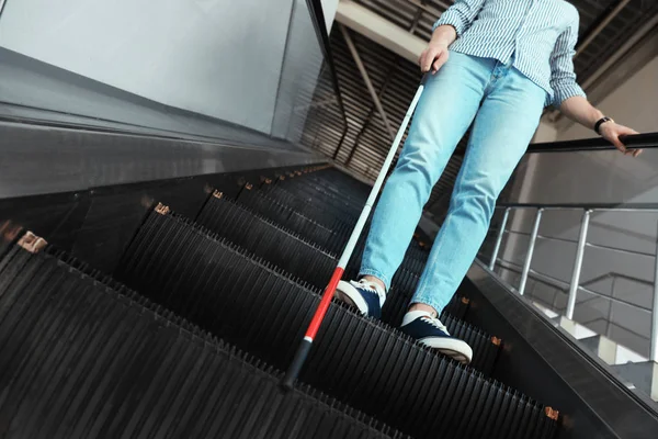 Blind person with long cane on escalator indoors