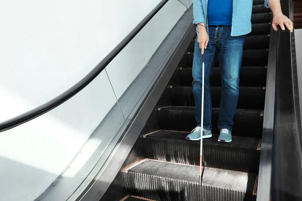 Blind person with long cane on escalator indoors. Space for text