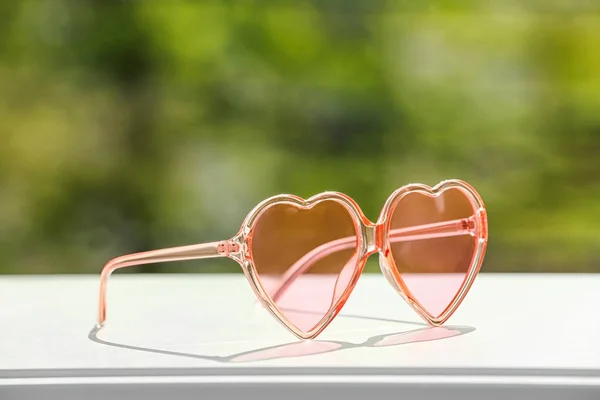 Κομψά γυαλιά ηλίου σε σχήμα καρδιάς στο τραπέζι από θολή φόντο. Χώρος για κείμενο — Φωτογραφία Αρχείου