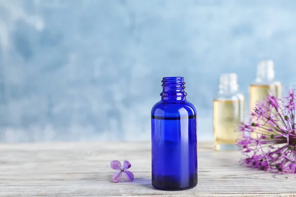 stock image Bottle of essential oil with flowers on wooden table against color background, space for text