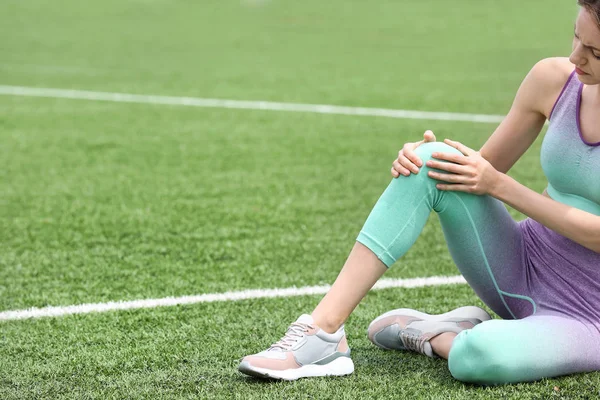 Femme en vêtements de sport souffrant de douleurs au genou sur le terrain de football, gros plan — Photo
