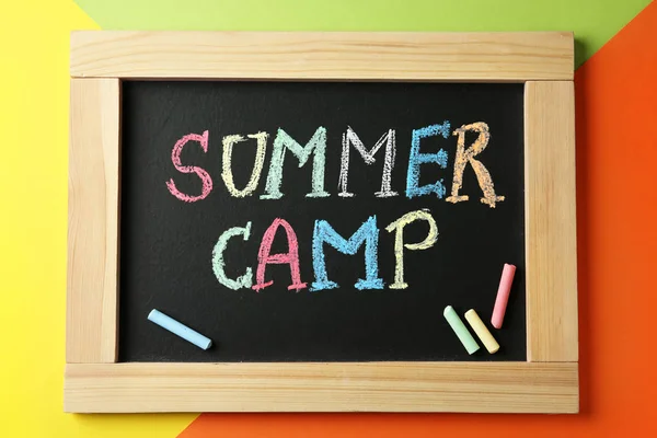Small blackboard with text SUMMER CAMP and chalk sticks on color background, top view — Stock Photo, Image