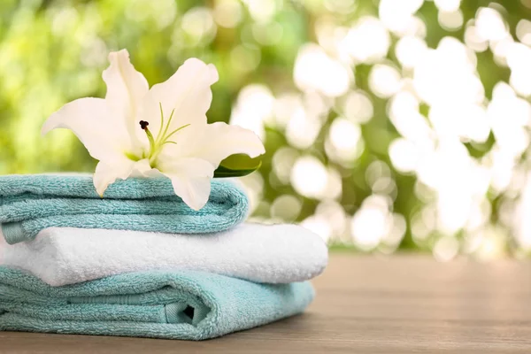 Stack of clean towels with lily on table against blurred background. Space for text — Stock Photo, Image