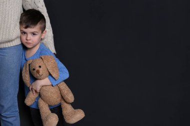 Siyah arka planda annesini kucaklıyor oyuncak ile Sad küçük çocuk, metin için boşluk