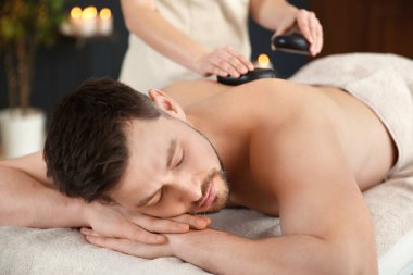 Yakışıklı adam spa salonunda sıcak taş masajı alan