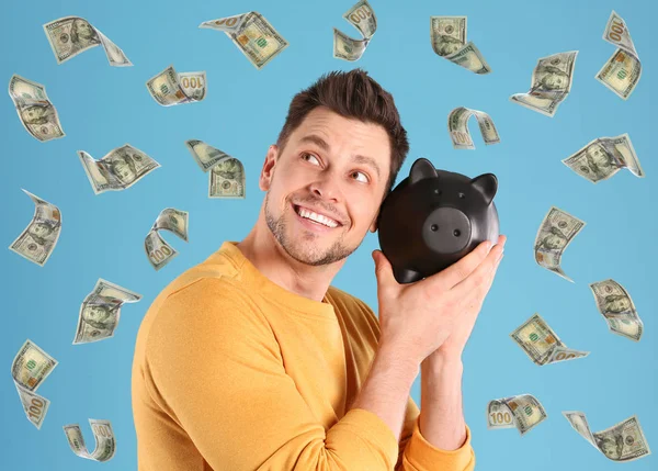 Happy man with piggy bank and flying money on color background — Stock Photo, Image