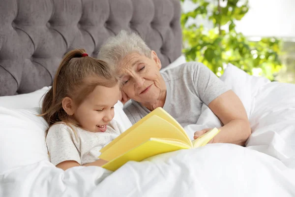 Fille mignonne et sa grand-mère lecture livre sur le lit à la maison — Photo