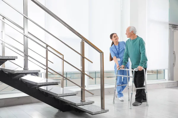 Enfermera asistiendo a hombre mayor con andador en el hospital —  Fotos de Stock