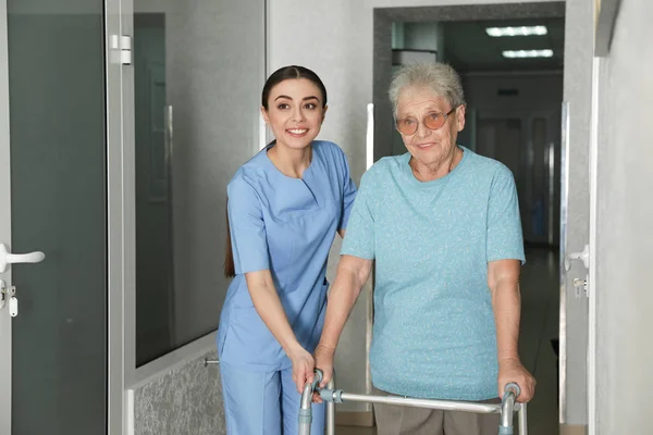 Νοσοκόμα βοηθώντας τον ανώτερο ασθενή με περιπατητή στο νοσοκομείο διάδρομο — Φωτογραφία Αρχείου