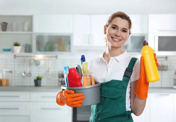 Retrato de mulher jovem com bacia de detergentes e garrafa na cozinha. Serviço de limpeza — Fotografia de Stock