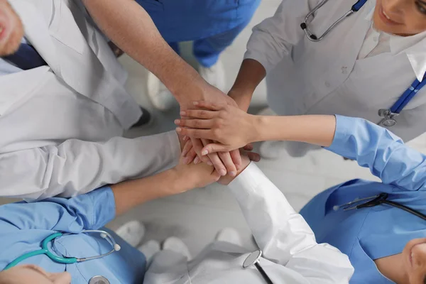 Молодые врачи держат руки в помещении, вид сверху. Концепция единства — стоковое фото