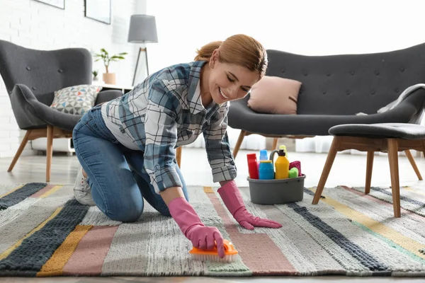 Portret kobiety sprzątanie dywan z pędzlem w salonie — Zdjęcie stockowe